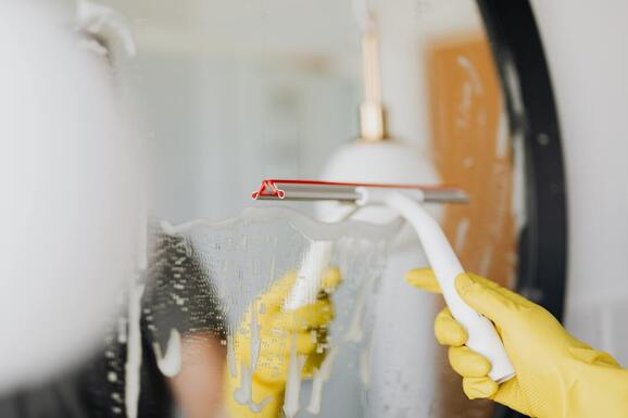 Picture of a cleaning service employee with yellow gloves cleaning a mirror