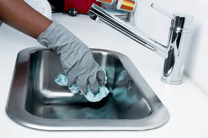 Picture of a cleaning service employee with gray gloves cleaning a bathroom sink
